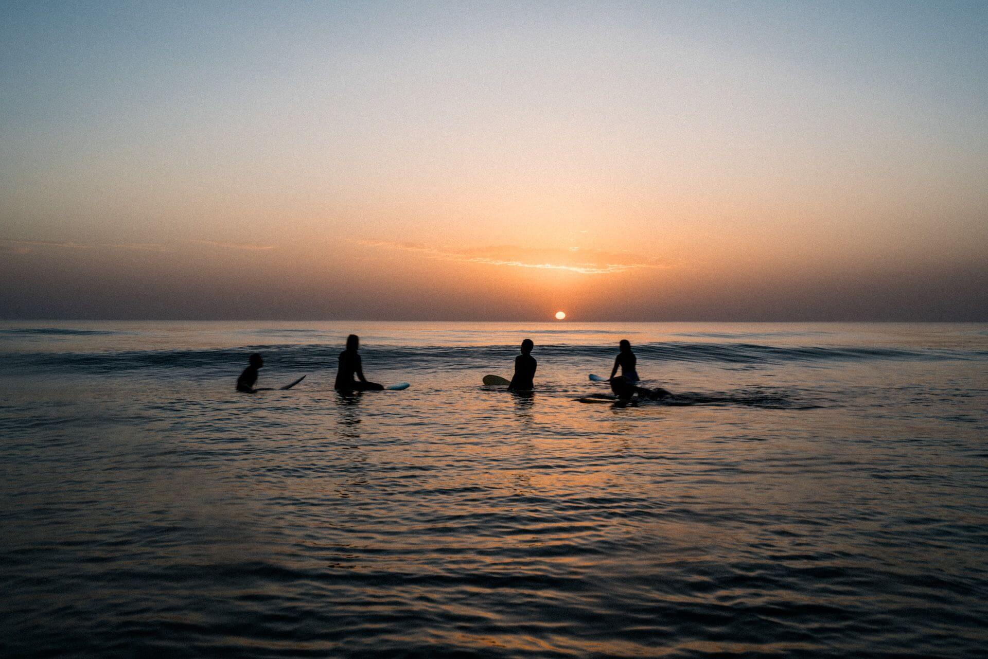 Silhouette of people watching beautiful sunset while floating in the sea with their surfboards